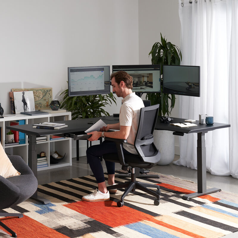 black finish l shape electric standing desk in a lowered position in the corner of a workspace image number null