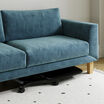 Close-up of the mobile laptop desk's low-profile tabletop and caster wheels tucked beneath a teal velvet sofa, demonstrating its ability to slide under furniture for storage.