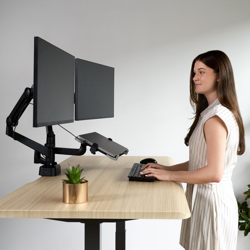 shows a person working in office environment with dual arm monitor and laptop stand image number null