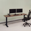 Electric standing desk 72x30 in walnut finish with black legs lowered in office