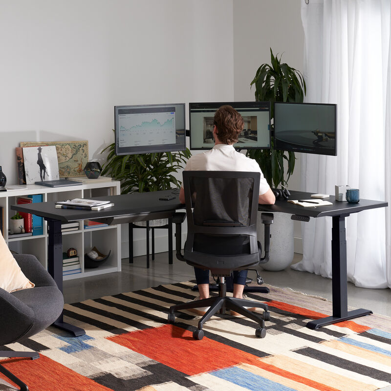 black finish l shape electric standing desk in a lowered position in the corner of a workspace image number null
