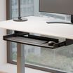side view of keyboard trey attached to desk with keyboard on white standing desk