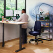 professional standing at desk with deep blue temper-pedic chair in a home office setting