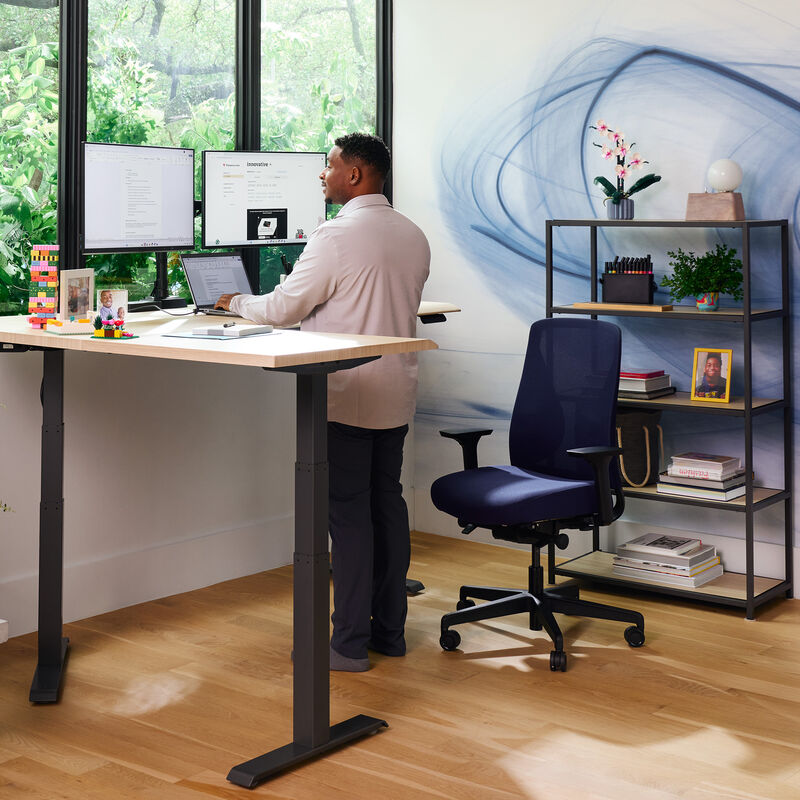 professional standing at desk with deep blue temper-pedic chair in a home office setting image number null