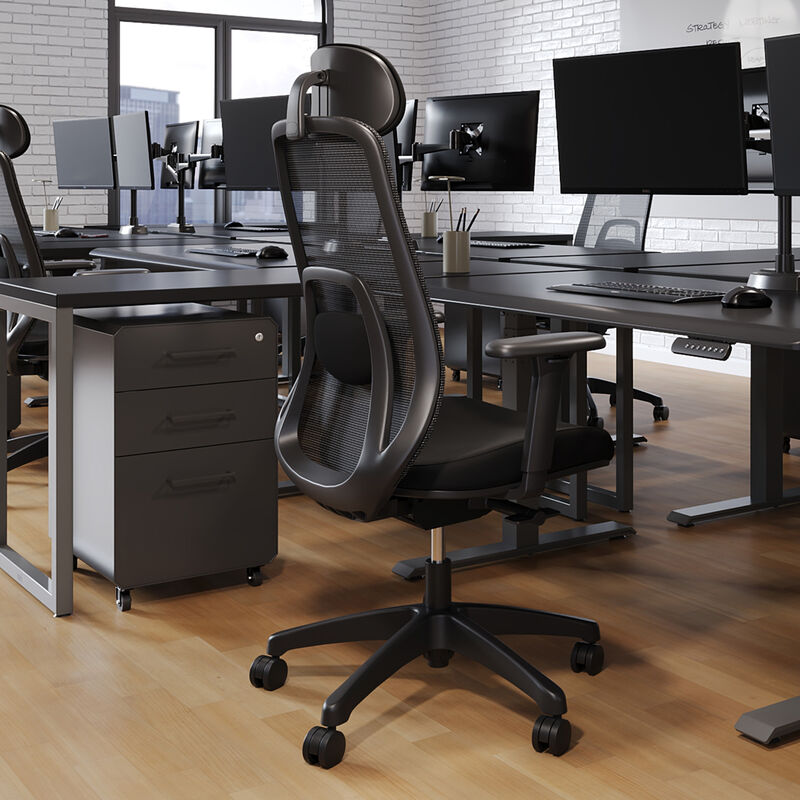 Rear angled view of a black mesh task chair showing the headrest, backrest frame, and armrests, positioned in an open office with desks and monitors in the background. image number null