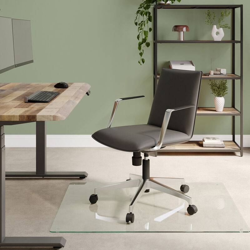 Modern office space with a sleek black ergonomic chair on casters, light wood flooring, large industrial windows, and minimalist furniture against an exposed brick wall backdrop. image number null