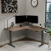 walnut finish l shape electric standing desk in a lowered position in the corner of a workspace