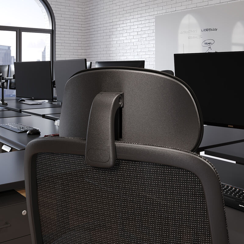 Close-up rear view of the black headrest mounted on a mesh office chair, showing the adjustable arm and mounting bracket, in an open office setting. image number null