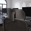 Close-up view of the chair's black headrest and upper mesh backrest showing the adjustable headrest mount, in an open office setting with desks and monitors.