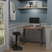 electric standing desk lowered in a stylish home office nook with a monitor, keyboard, and ergonomic stool.
