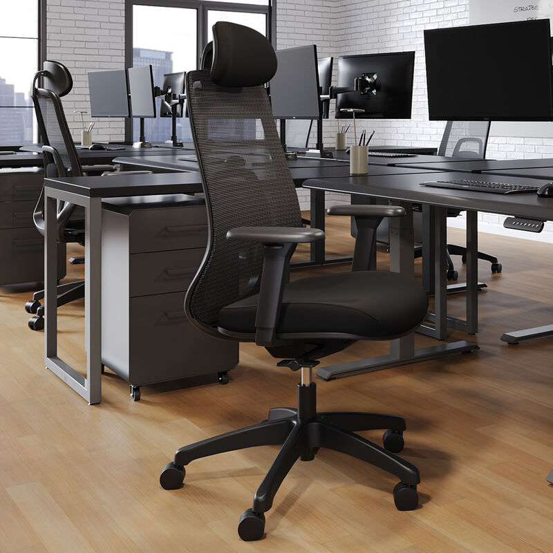 Front angled view of a black mesh task chair with an adjustable headrest, armrests, and a five-star caster base, shown in an open office with desks and monitors in the background. image number null