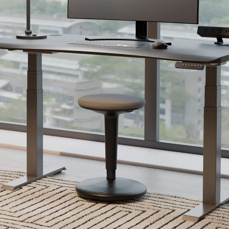 balance stool sitting in front of an electric standing desk in a office in a raised position image number null