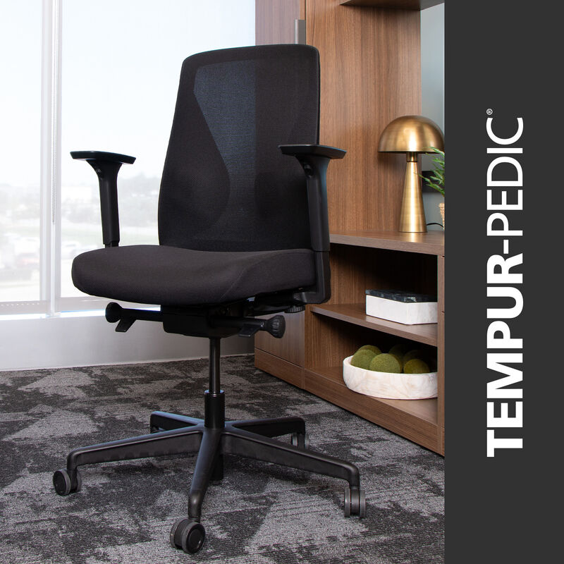 Black ergonomic Tempur-Pedic office chair from Vari with mesh back and adjustable armrests, shown in a modern office setting with wood shelving and decorative accents image number null
