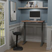 walnut electric standing desk raised in a stylish home office nook with a monitor, keyboard, and ergonomic stool.