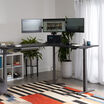 black finish l shape electric standing desk in a raised position in the corner of a workspace