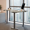 driftwood electric standing desktop with slate legs in an office setting in a raised position