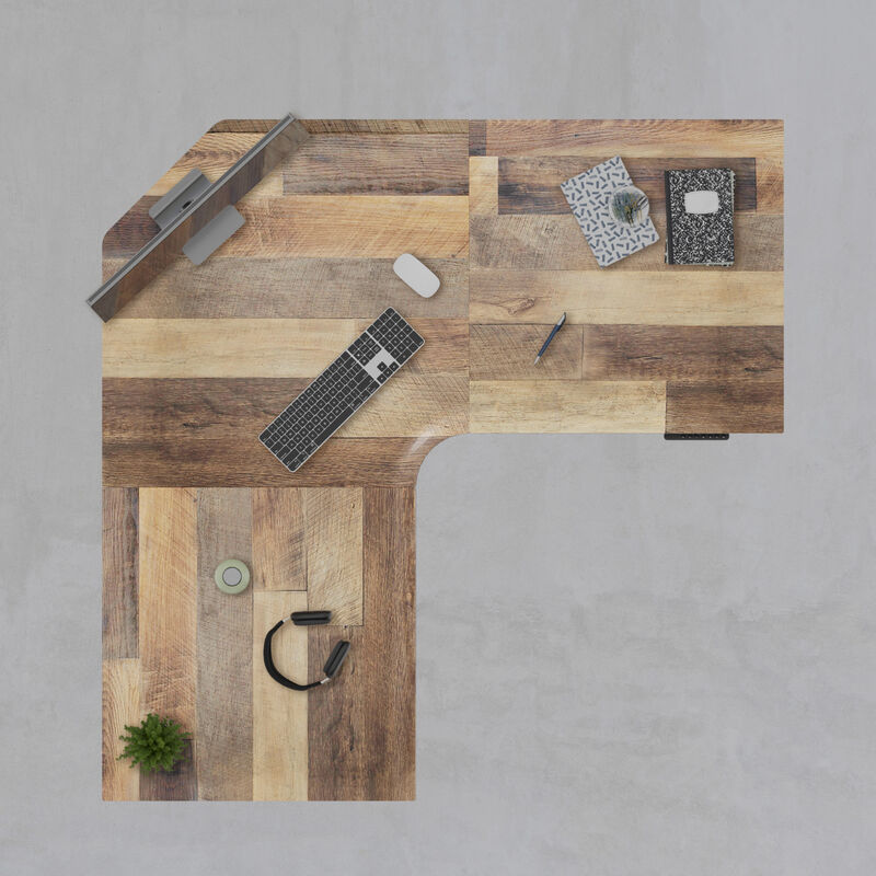 Top-down view of an L-shaped reclaimed wood-look desktop with a monitor, keyboard, mouse, notebooks, pen, headphones, and a small plant, on a gray concrete floor. image number null