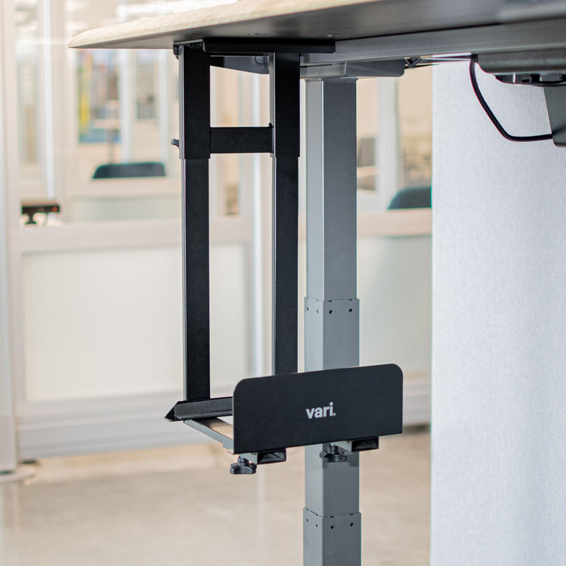 Empty Vari PC desk mount installed under a desk in a modern office setting, showing its adjustable frame and clamping mechanism ready to hold a computer tower securely off the floor. image number null