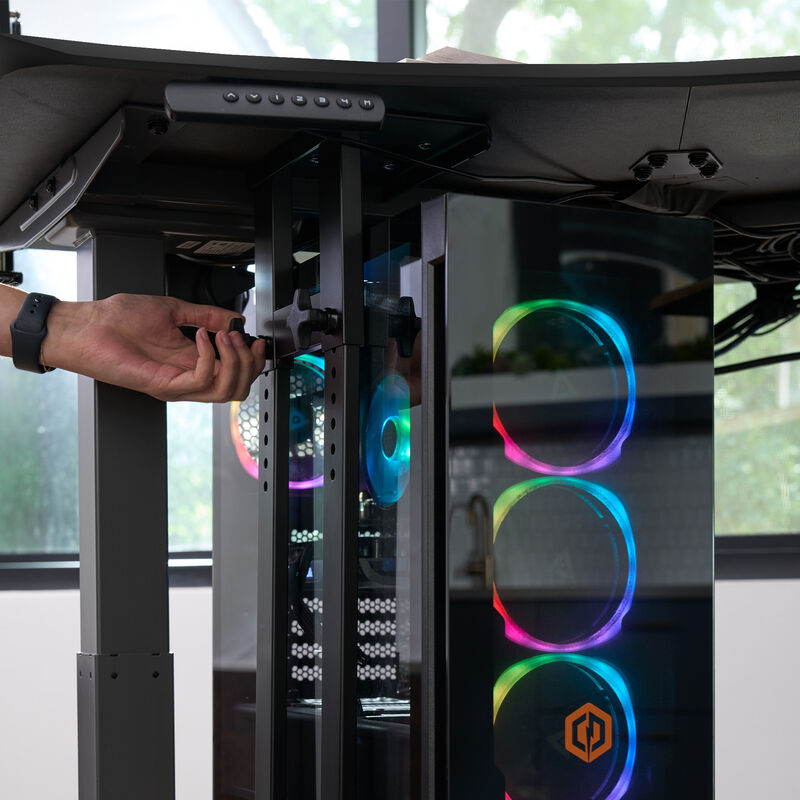 A gaming PC mounted under a sit-stand desk using a black Vari desk mount; RGB lighting is visible inside the PC case. image number null