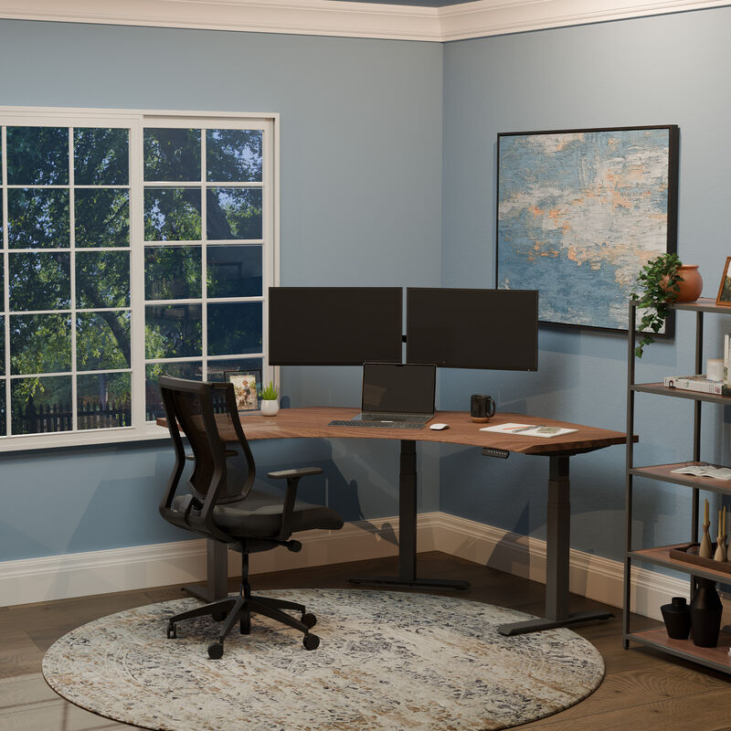 A clean and modern home office setup with a dark wood L-shaped standing desk, dual monitors, mesh ergonomic chair, and blue walls accented by large windows and abstract wall art. image number null