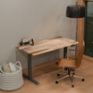 Reclaimed wood TechTrack ESD desk with a black frame in a home office corner, sitting, styled with a flip clock, phone stand, cognac leather office chair, floor lamp, and a woven basket with pillows.