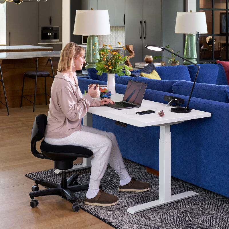 woman sitting at a desk, working on a laptop while holding a mug sitting on the core chair image number null