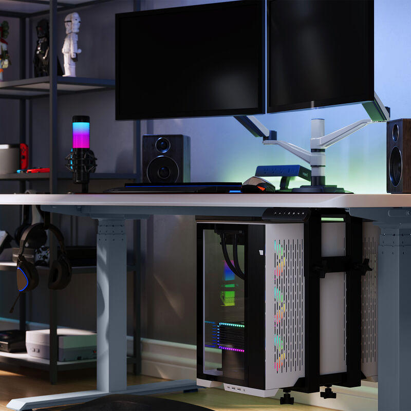 A gaming PC mounted under a desk using a Vari mount, with dual monitors, speakers, and RGB-lit accessories on the desk; shelving with tech gear and collectibles is visible in the background. image number null