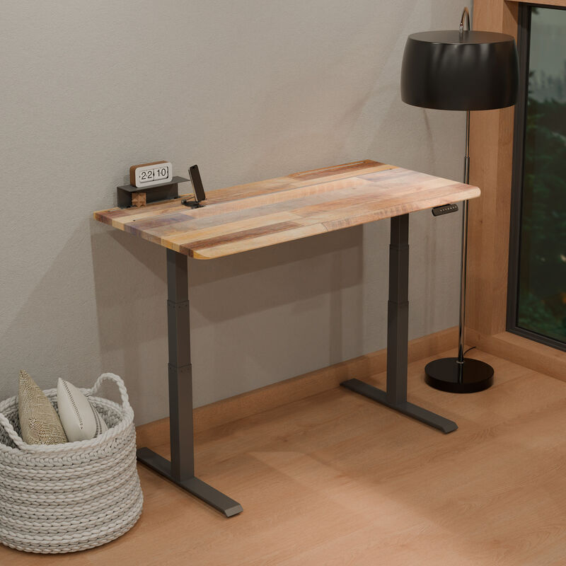Reclaimed wood TechTrack ESD desk with a black frame in a home office corner, standing, styled with a flip clock, phone stand, cognac leather office chair, floor lamp, and a woven basket with pillows. image number null