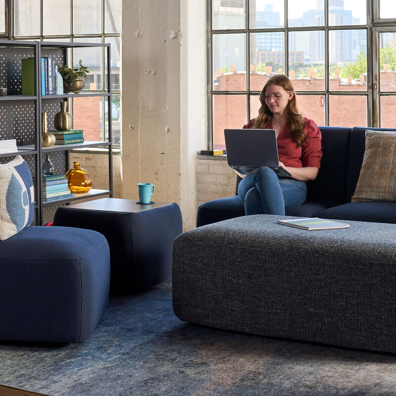 woman sitting on a couch working on her laptop in an open office image number null