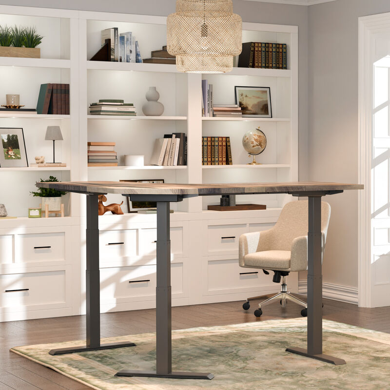 L-shaped standing desk with a reclaimed wood-look top and dark gray legs, with a beige chair to the side, in a home office with white built-in shelves and drawers. image number null