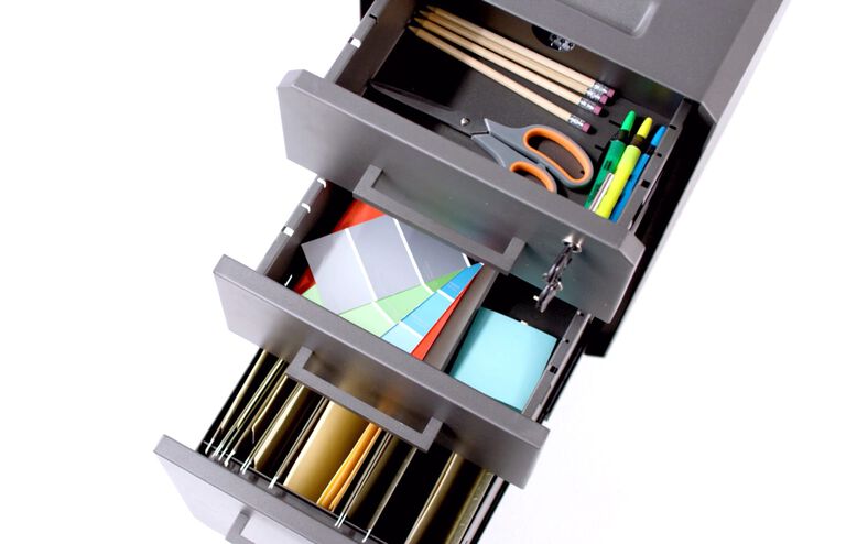Slim File Cabinet is seen from above with all three drawers open, the bottom has hanging files, and the two uppper drawers have colorful office accessories. 