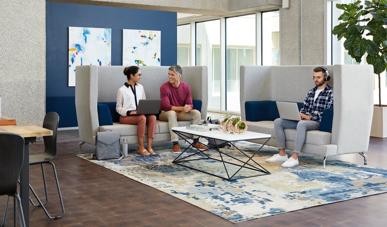interior of Las Colinas locations, with tall ceilings and three professionals working on soft seating. 
