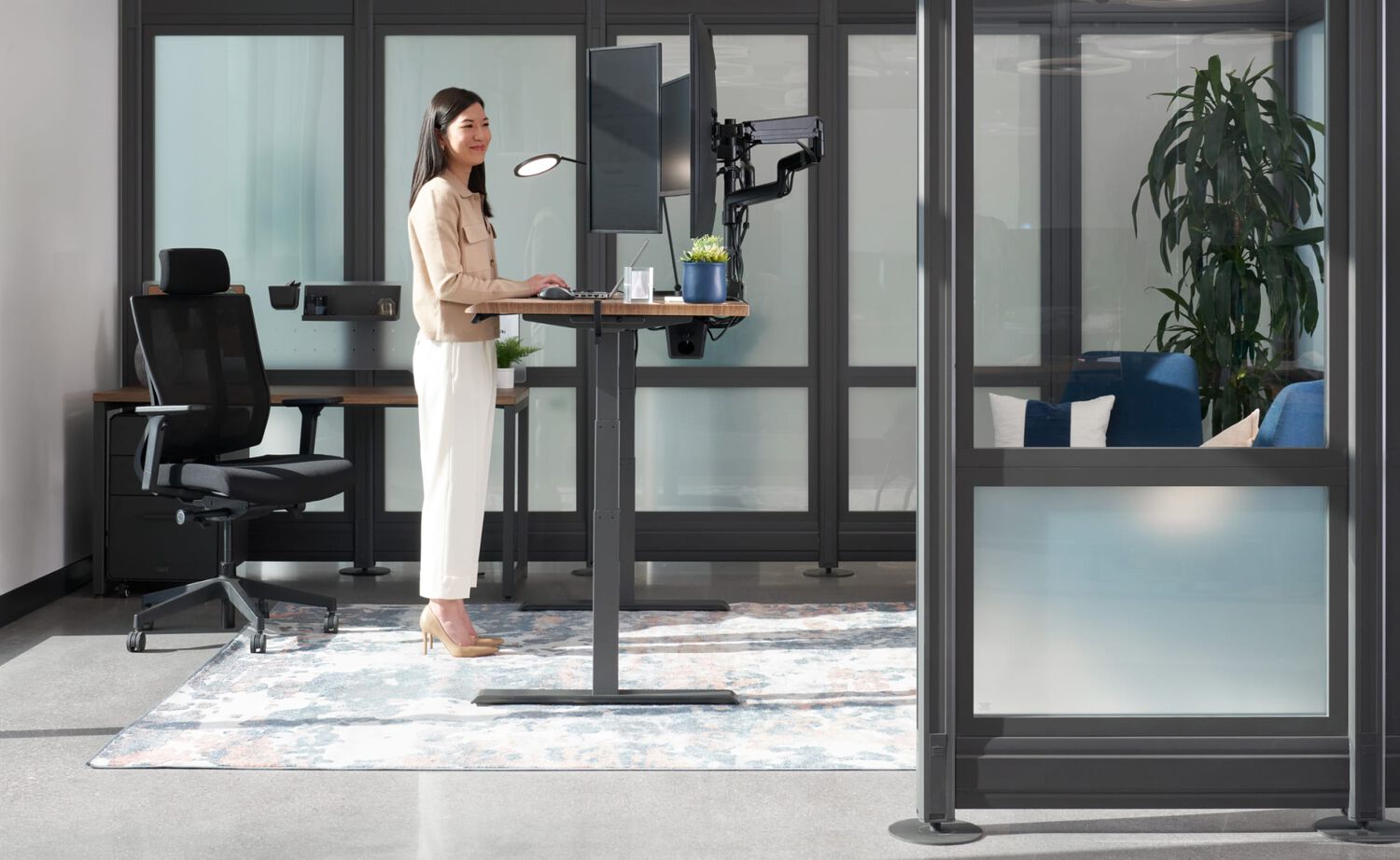 professional working at a Vari electric standing desk with monitor arm and laptop stand displays and a task chair in a home office setting