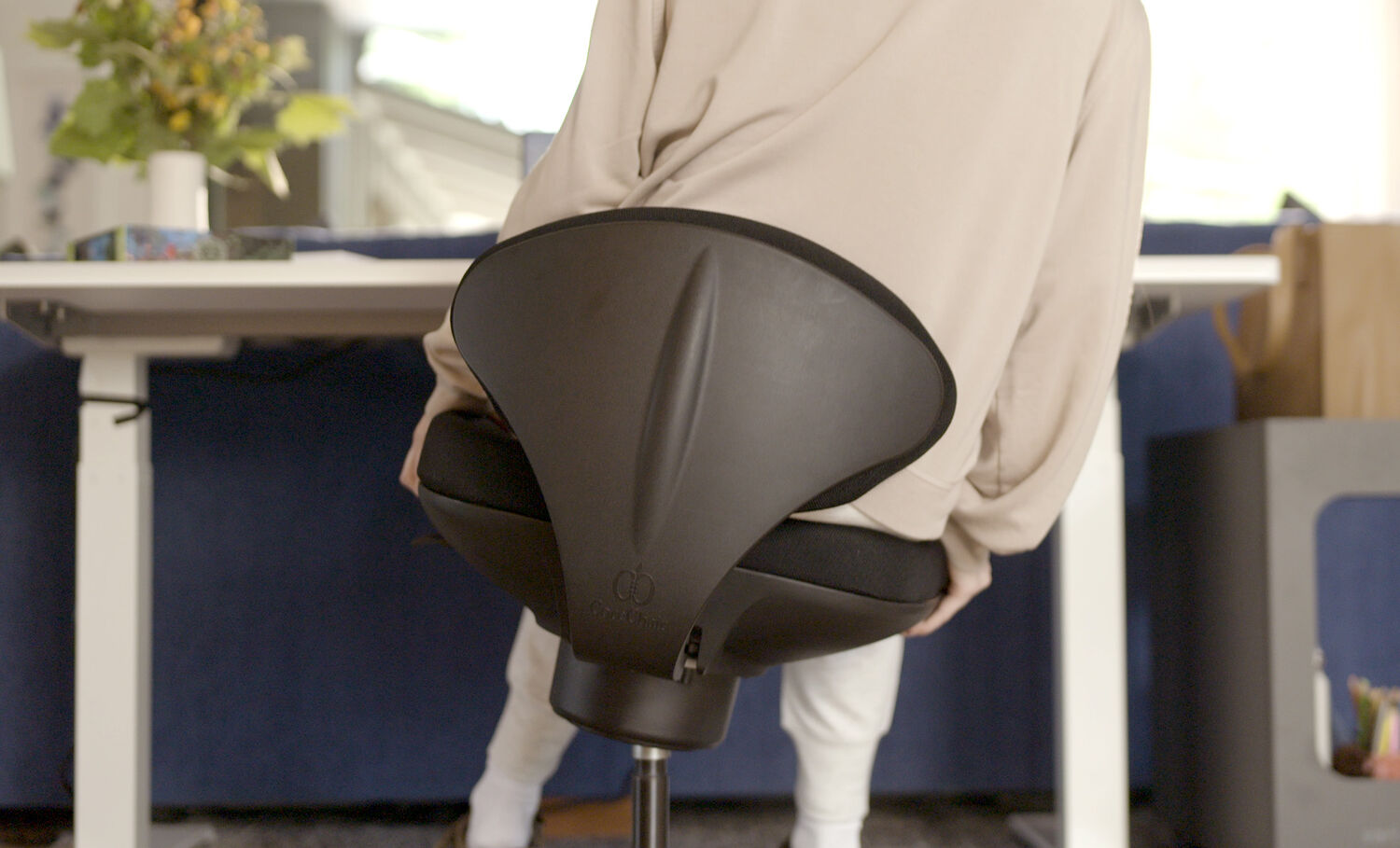Close-up of a hand pressing into the black seat cushion, showing the material's softness and support, with a branded fabric tag visible on the textured surface.