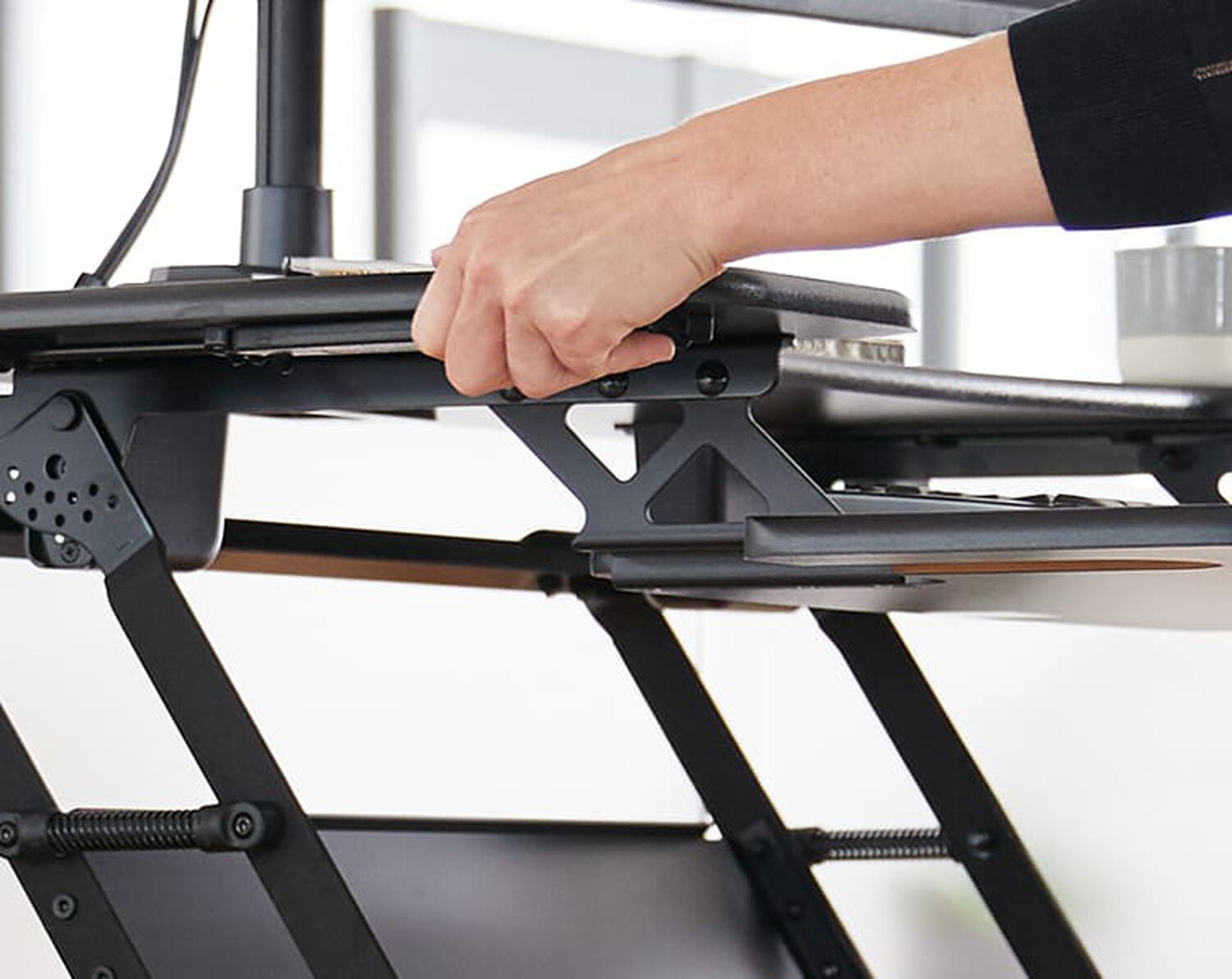 Desk converter lowered to sitting position with a sinle monitor arm mounted on it in an office setting
