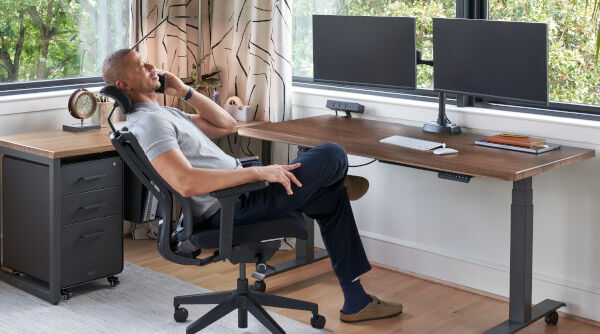 person sitting in a vari task chair with headrest next to a vari electric standing desk