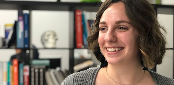individual smiling and standing in front of bookcase