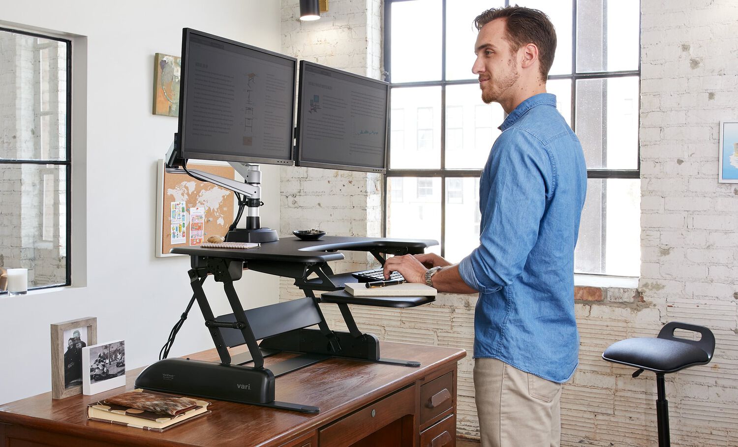 Individual standing at varidesk converter on top of existing desk in office