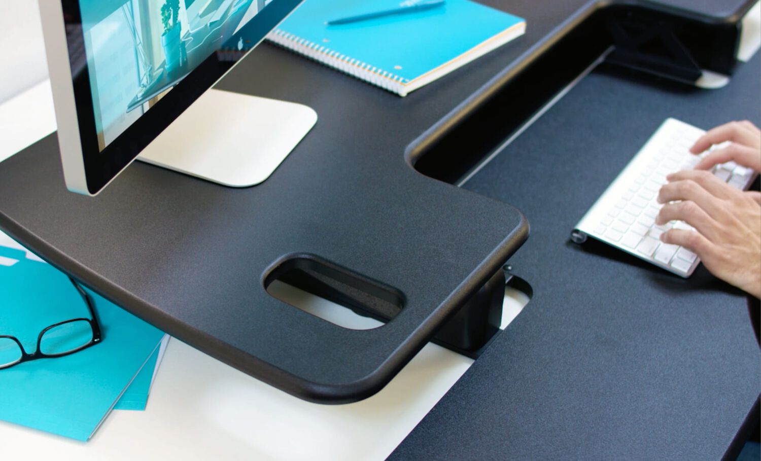 Individual typing on keyboard located on the keyboard tray of the desktop riser