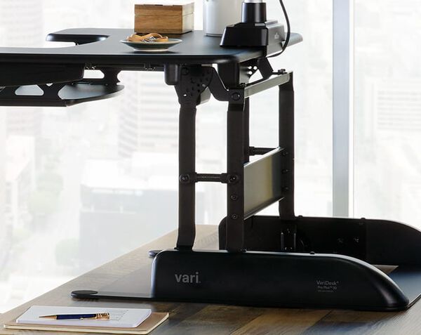 Desk riser raised to max height with a focus on the weighted base of the converter