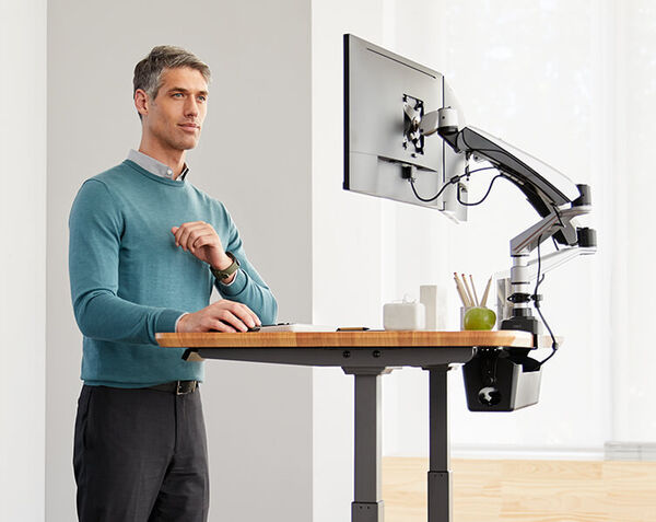 professional working at electric standing desk with cable management tray and monitor arms