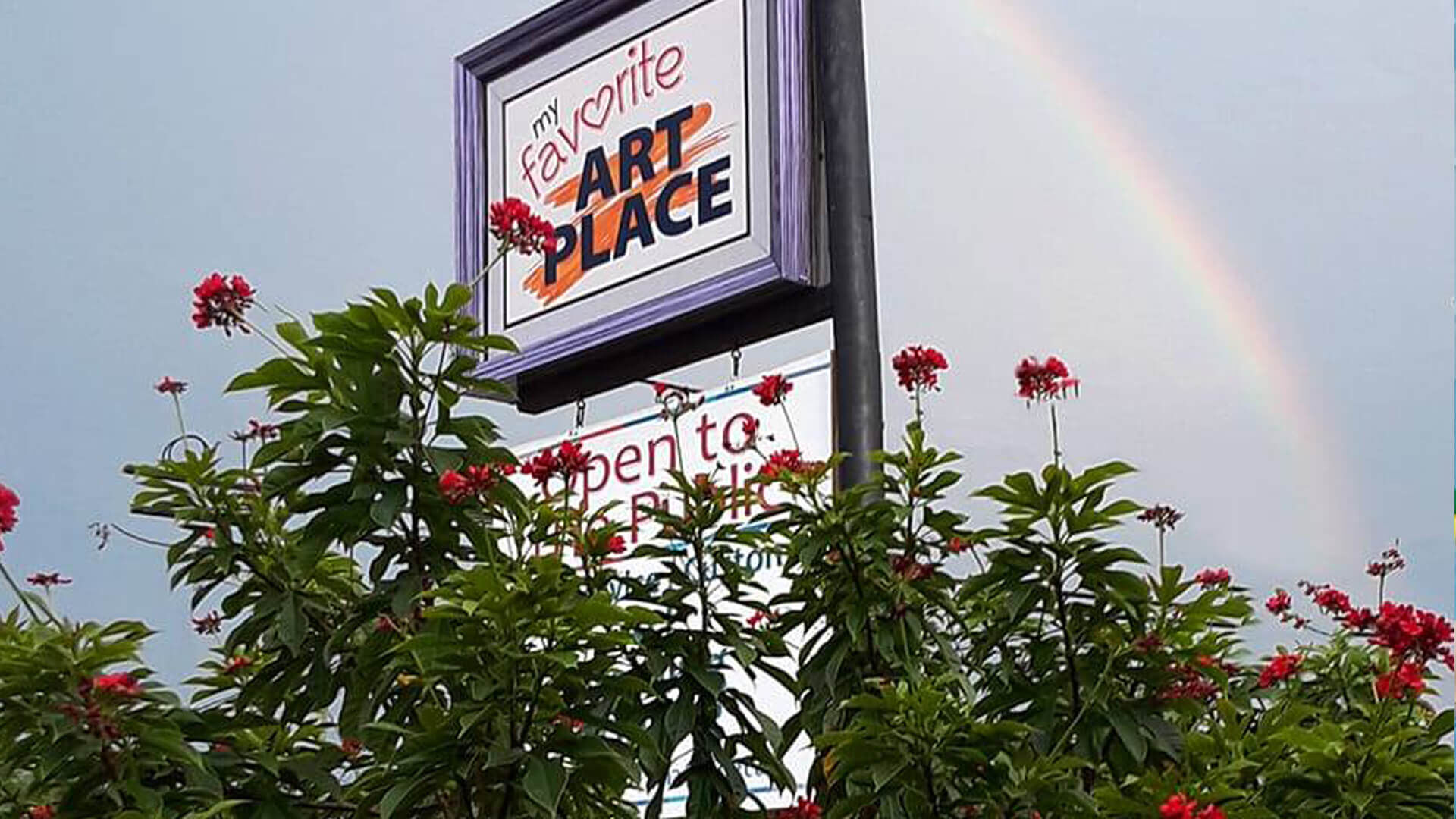 my favorite art place's sign with a flower bush in front 