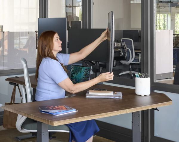 individual adjusting a monitor while working at a desk
