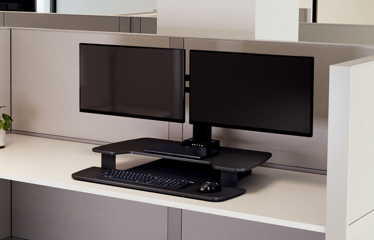 premier electric dual-monitor in a lowered position setup on a desk in a cubicle 