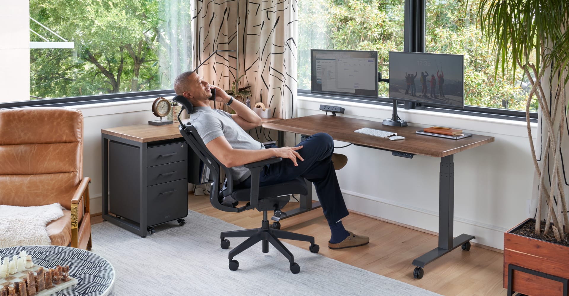 an individuals leaning back in an office chair while on the phone in his home office