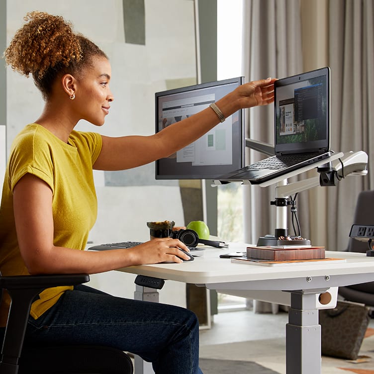 professional seated at electric standing desk adjusting mounted laptop