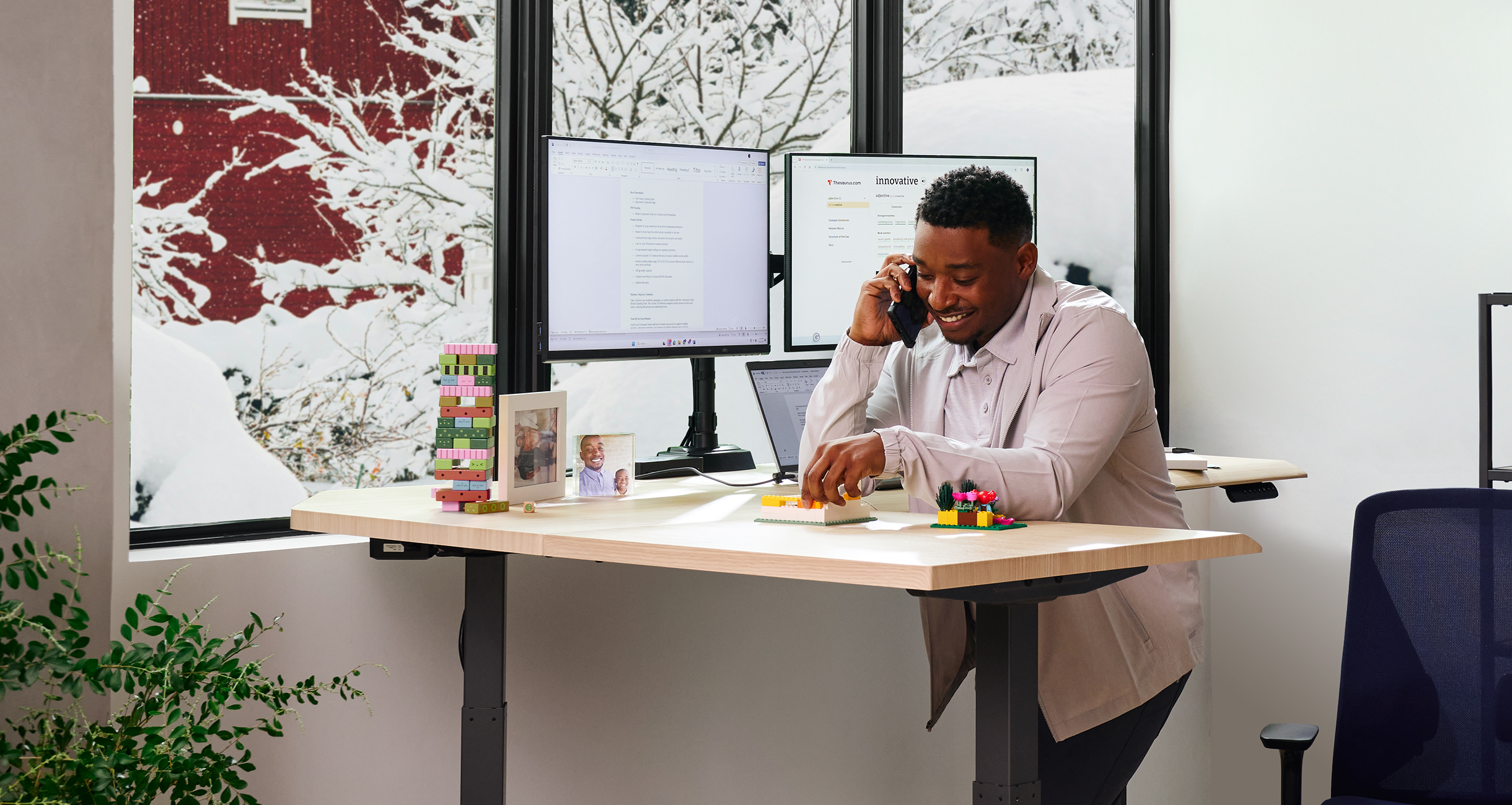 man leaning on an L shape electric standing desk while on the phone