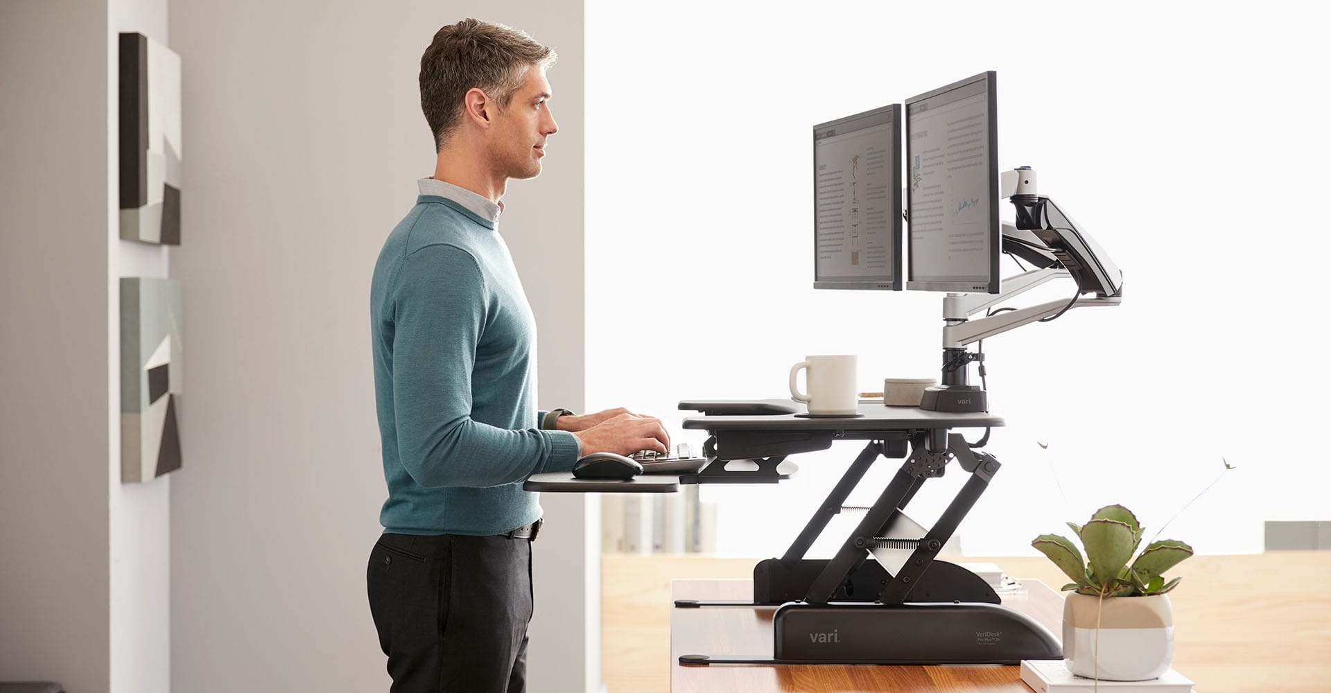 individual working at an electric standing desk and dual monitor arms